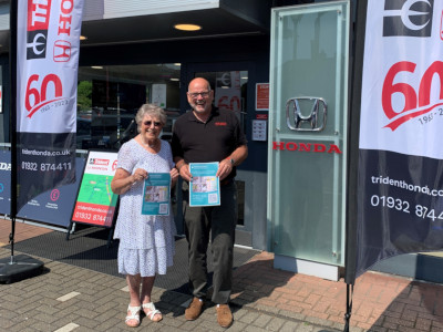 Mrs Thelma Forbes and Richard Roberts, Managing Director of Trident Honda, standing in front of our Ottershaw showroom, holding her sponsorship posters